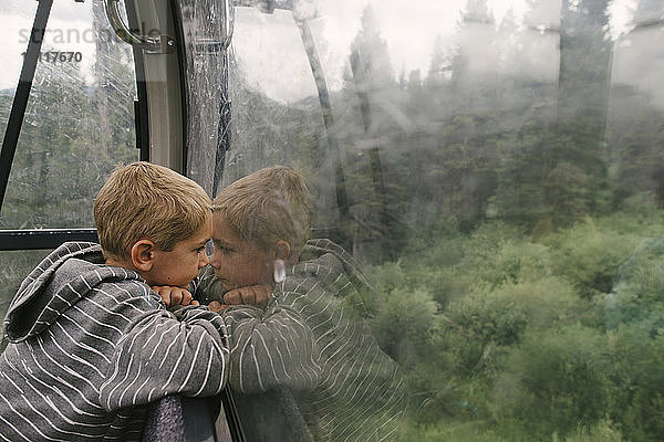 Seitenansicht eines Jungen  der durch ein Fenster schaut  während er in der Luftseilbahn fährt
