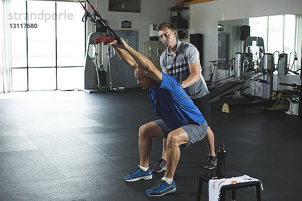 Trainer  der einem Mann beim Üben von Dehnungsübungen mit Widerstandsband im Fitnessstudio assistiert