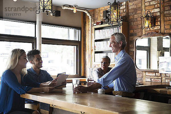 Männlicher Besitzer serviert Getränke  während er sich mit Kunden an der Bartheke im Café unterhält