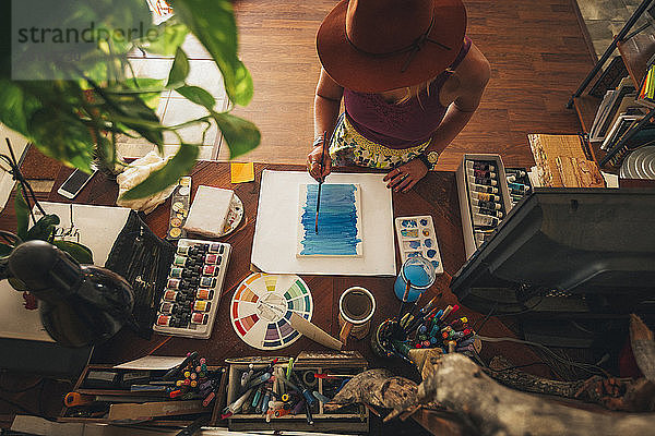 Hochwinkelansicht eines Künstlers  der zu Hause stehend auf einem Tisch malt