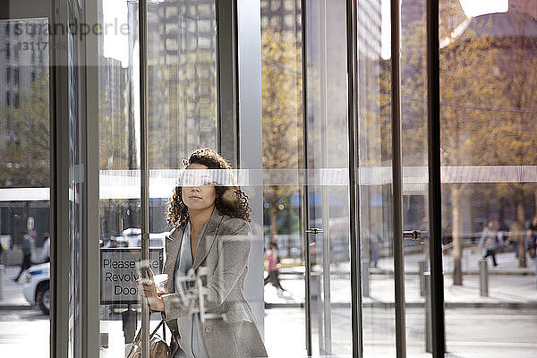 Geschäftsfrau öffnet Karusselltür beim Betreten eines modernen Gebäudes