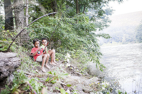 Geschwister beim Angeln  während sie am See im Wald sitzen