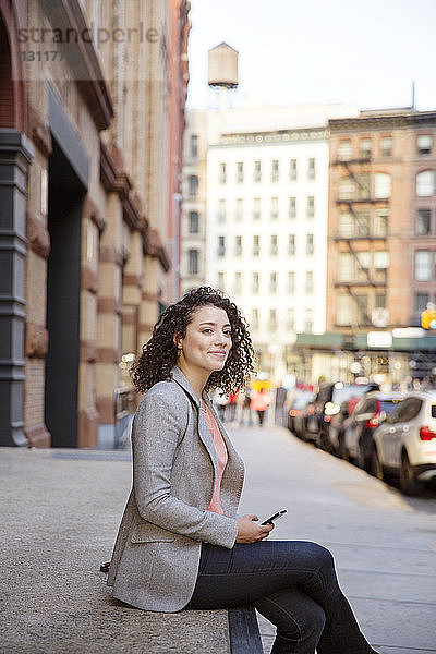 Seitenansicht einer nachdenklichen Geschäftsfrau  die auf dem Bürgersteig sitzt