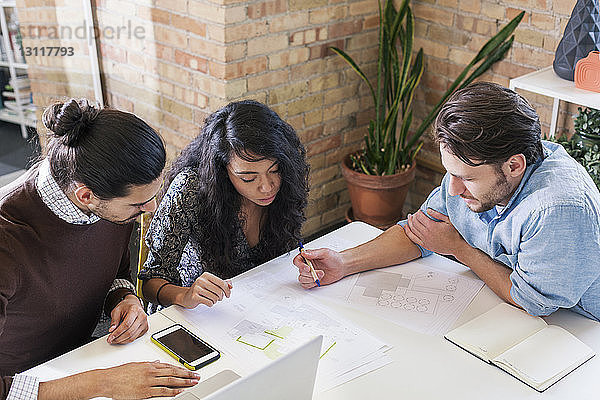 Schrägansicht von Geschäftsleuten  die einen Plan diskutieren  während sie im Büro am Schreibtisch sitzen