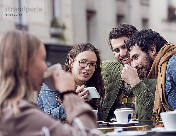 Glückliche Frau zeigt männlichen Freunden im Straßencafé ihr Smartphone