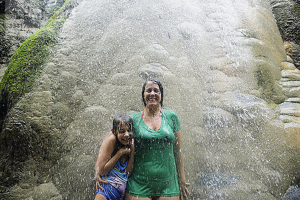 Glückliche Frau mit Tochter steht an Felsen bei den Bua-Thang-Wasserfällen