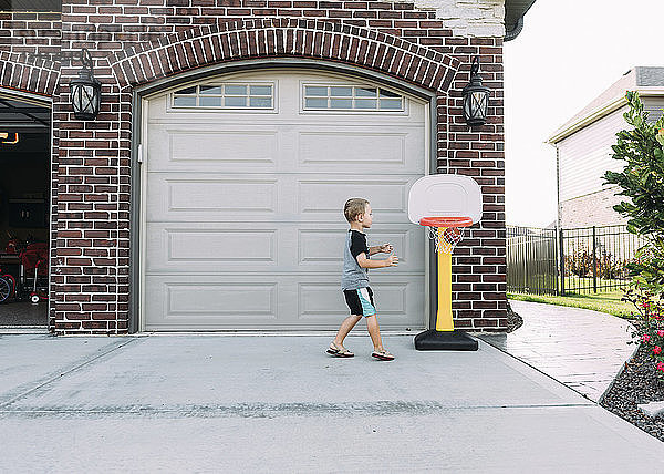 Glücklicher Junge spielt Basketball auf Einfahrt