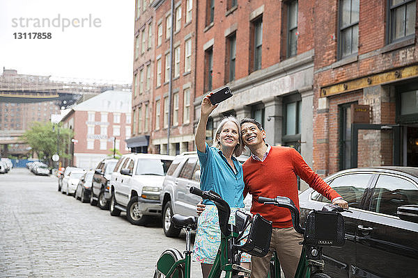 Glückliches reifes Paar  das sich beim Stehen mit Fahrrädern auf der Straße in der Stadt selbstständig macht