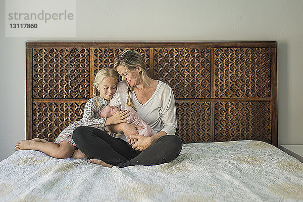 Mutter und Tochter sehen das Neugeborene im Sitzen im Bett an