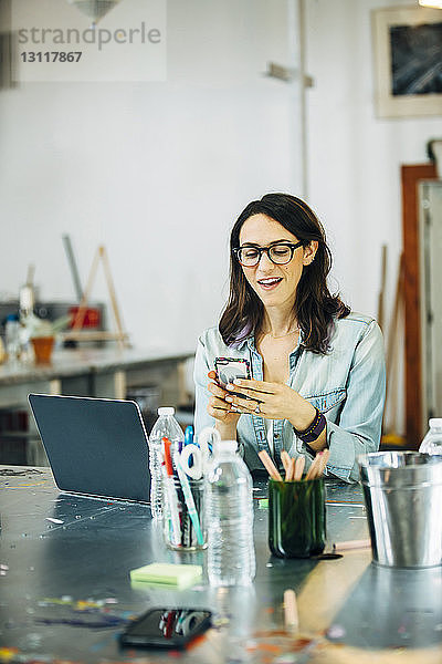 Glückliche Geschäftsfrau benutzt Smartphone bei der Arbeit im Büro