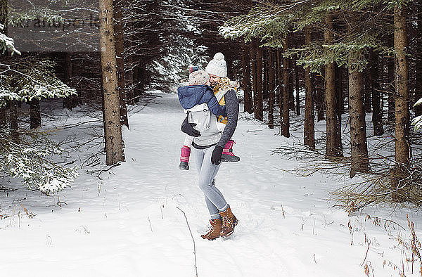 Glückliche Mutter mit Tochter im Winter im Wald stehend