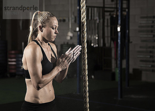 Seitenansicht einer Athletin  die vor dem Training im Fitnessstudio ihre Hände mit Kreide einstreicht