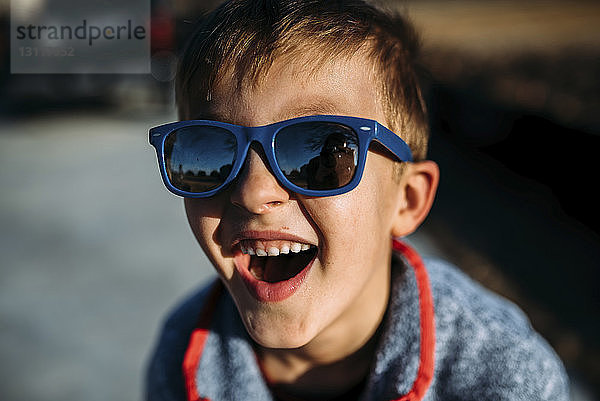 Hochwinkel-Nahaufnahme eines glücklichen Jungen  der eine Sonnenbrille trägt  während er im Freien sitzt