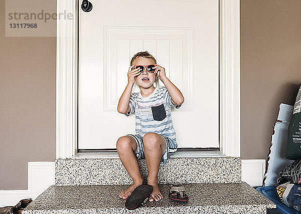 Junge trägt Sonnenbrille  während er auf der Türschwelle sitzt