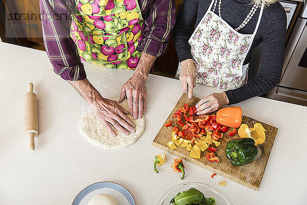 Mitschnitt einer Frau  die Paprika schneidet  während ein Mann zu Hause in der Küche Pizzateig herstellt