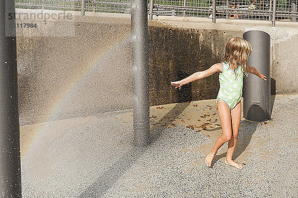 Verspieltes Mädchen genießt an einem sonnigen Tag Sommerferien im Springbrunnen