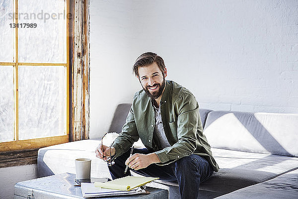 Porträt eines lächelnden Geschäftsmannes  der in einem Buch schreibt  während er im Kreativbüro sitzt