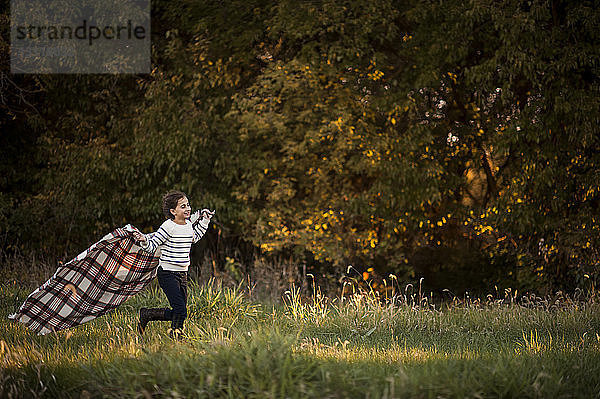 Verspieltes Mädchen hält beim Laufen im Park eine Picknickdecke