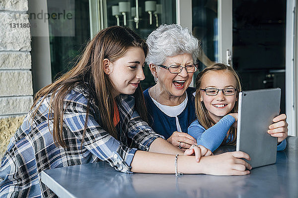 Glückliche Enkeltöchter und Großmutter mit Tablet-Computer auf der Veranda