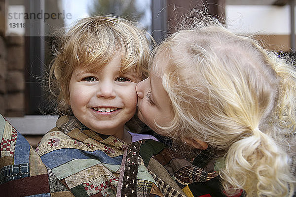 Porträt eines glücklichen Mädchens  während seine Schwester sie küsst