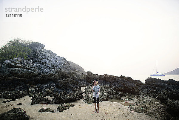 Mädchen in voller Länge auf Sand stehend an Felsen am Strand gegen den Himmel