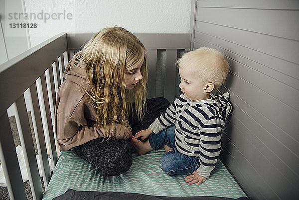 Mädchen mit Bruder sitzt zu Hause in der Krippe