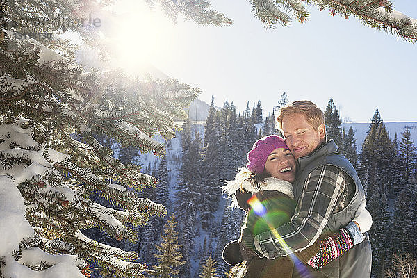 Paar umarmt sich  während es im verschneiten Wald vor klarem Himmel steht