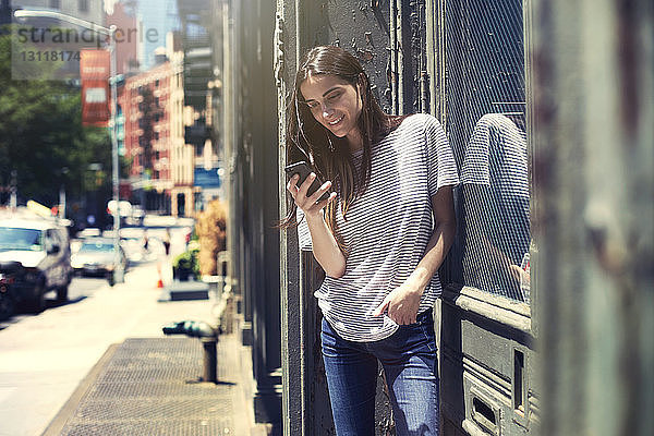 Lächelnde Frau benutzt Smartphone an einem sonnigen Tag