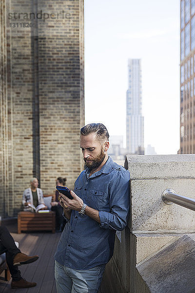 Mann benutzt Mobiltelefon  während Kollegen im Hintergrund sitzen