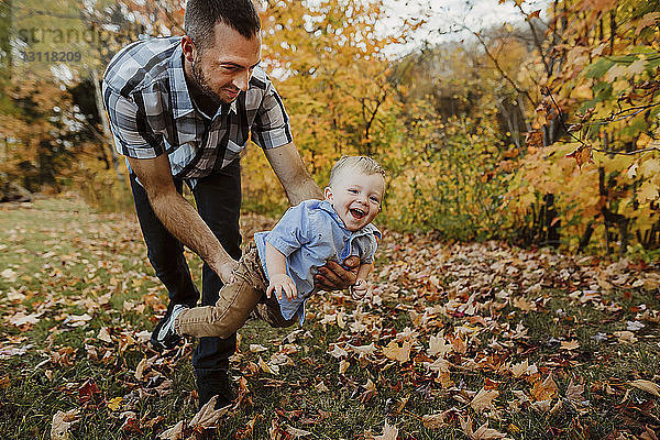 Vater spielt mit dem Sohn  während er im Herbst auf einem Grasfeld im Wald steht