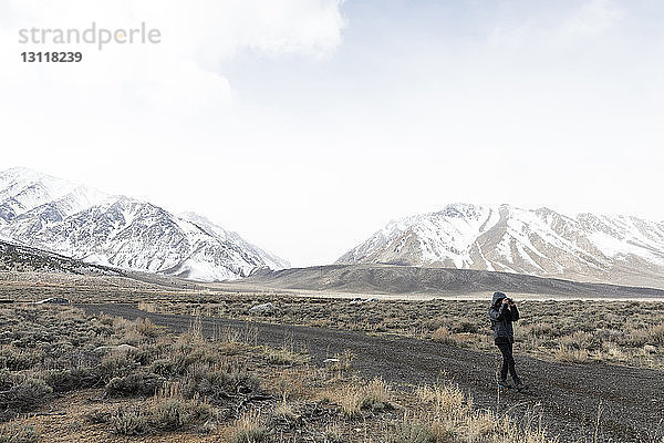 Mann fotografiert beim Gehen auf unbefestigter Straße am Mammoth Mountain