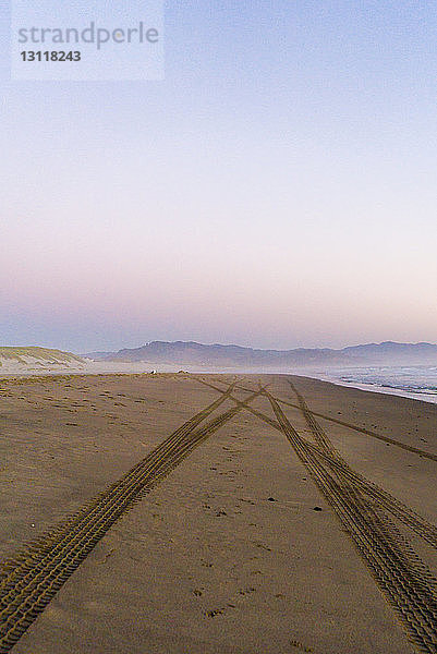 Reifenspuren auf Sand am Strand gegen klaren Himmel bei Sonnenuntergang
