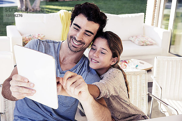 Glücklicher Vater und Tochter benutzen digitales Tablet  während sie auf einem Stuhl sitzen