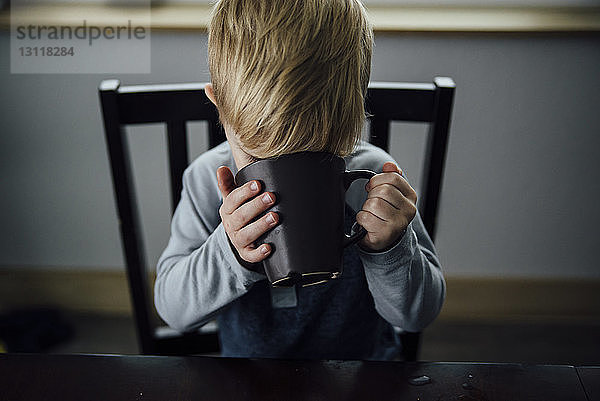 Schrägaufnahme eines Jungen  der zu Hause auf einem Stuhl sitzt und trinkt