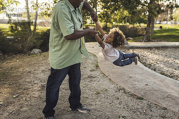 Mitschnitt eines spielerischen Vaters  der seinen Sohn beim Spielen im Park schwingt