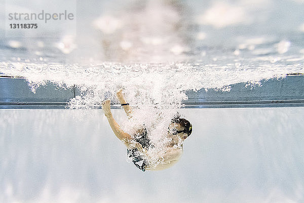 Junge ohne Hemd schwimmt in voller Länge unter Wasser im Pool