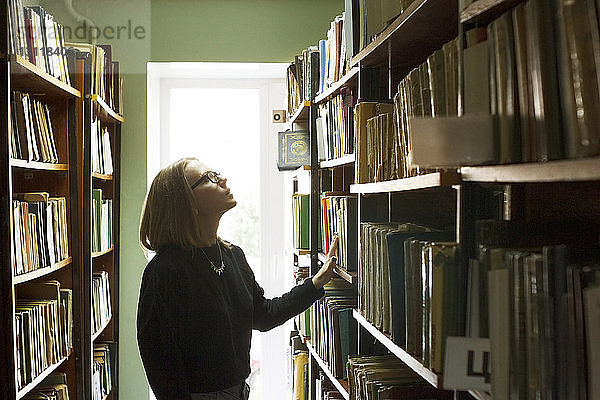 Seitenansicht einer Frau  die Bücher auswählt  während sie in der Bibliothek steht
