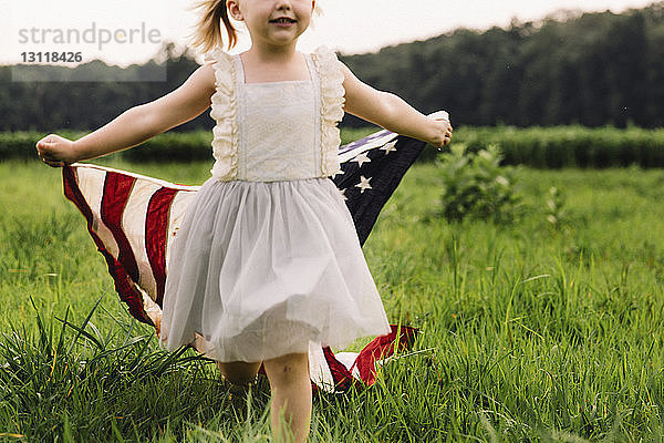 Mädchen mit amerikanischer Flagge in der Mitte beim Gehen auf Grasfeld