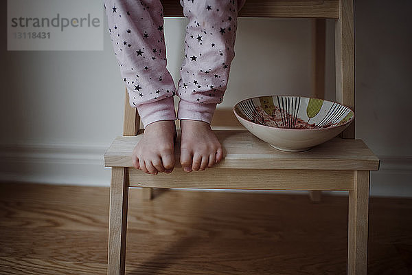 Niedrige Sektion eines Mädchens  das mit Schale auf Holzstuhl zu Hause steht