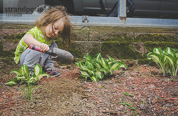 Mädchen gräbt Erde mit Kelle  während sie im Garten kauert