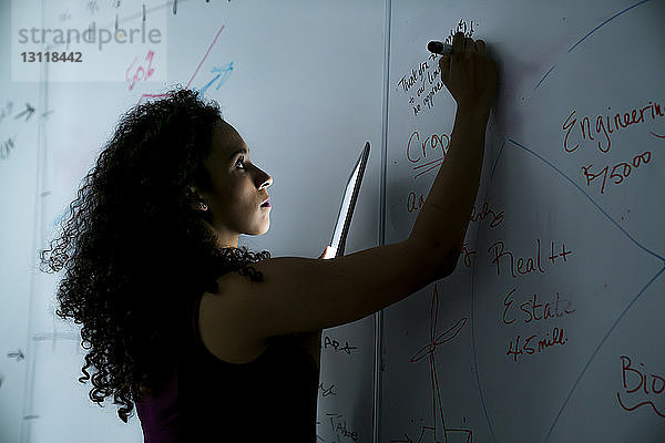 Geschäftsfrau schreibt im Büro auf Whiteboard über Tablet-Computer