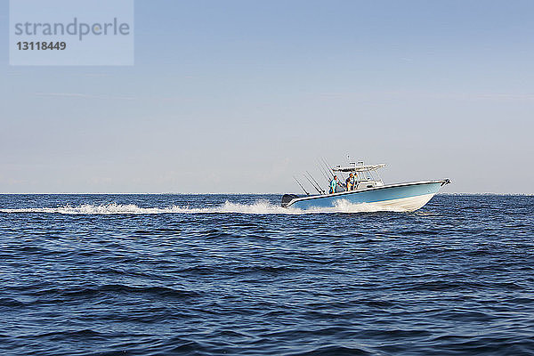 Freunde reisen auf einem Fischerboot auf See gegen den klaren Himmel