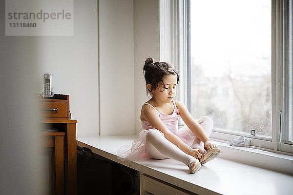 Mädchen in Ballettschuhen  das zu Hause am Tisch am Fenster sitzt