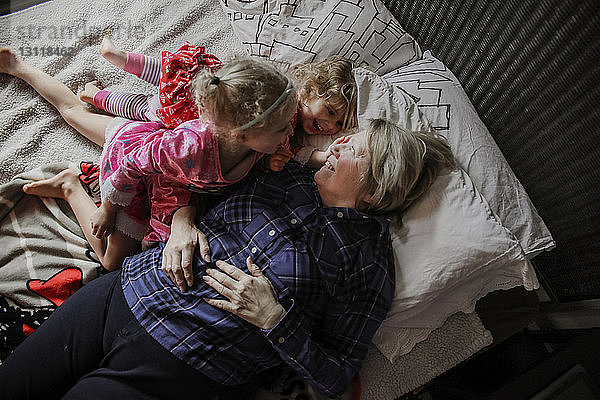 Draufsicht auf glückliche Enkelinnen mit Großmutter im Bett