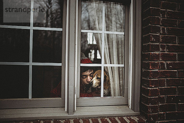 Teenager mit Hund zu Hause durch Fenster gesehen