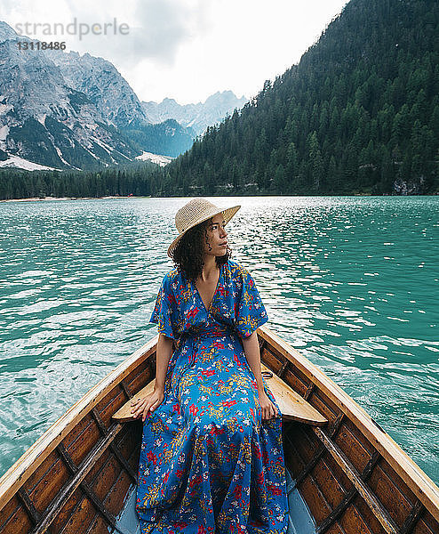 Junge Frau betrachtet Aussicht  während sie im Boot auf dem See vor Bergen sitzt
