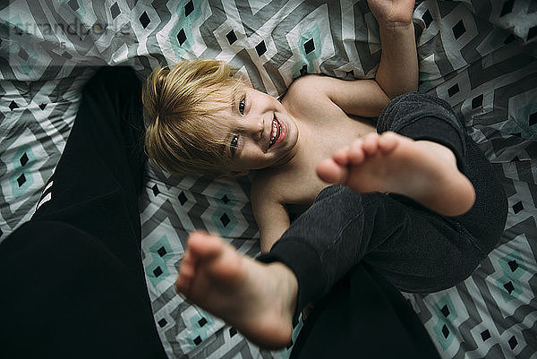 Portrait eines fröhlichen Jungen  der zu Hause auf dem Bett spielt