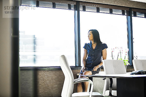 Nachdenkliche Geschäftsfrau schaut durch das Fenster  während sie im Büro sitzt