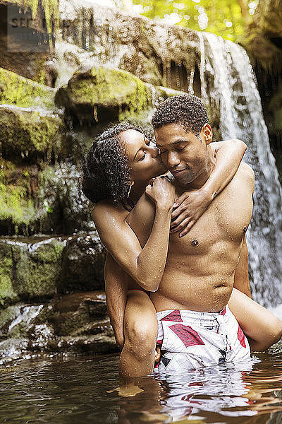Mann nimmt Frau huckepack und küsst sich im Fluss am Wasserfall