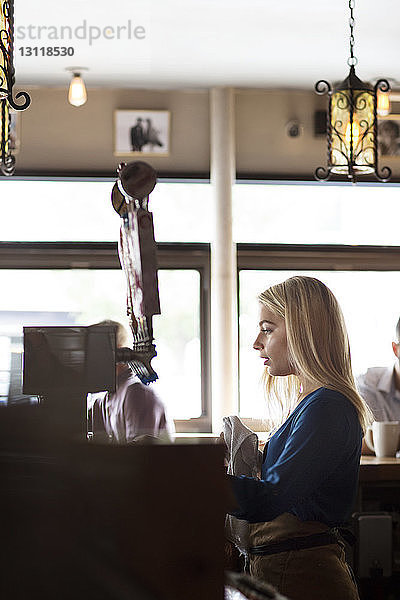 Seitenansicht einer Frau  die von Kunden im Cafe an der Theke steht